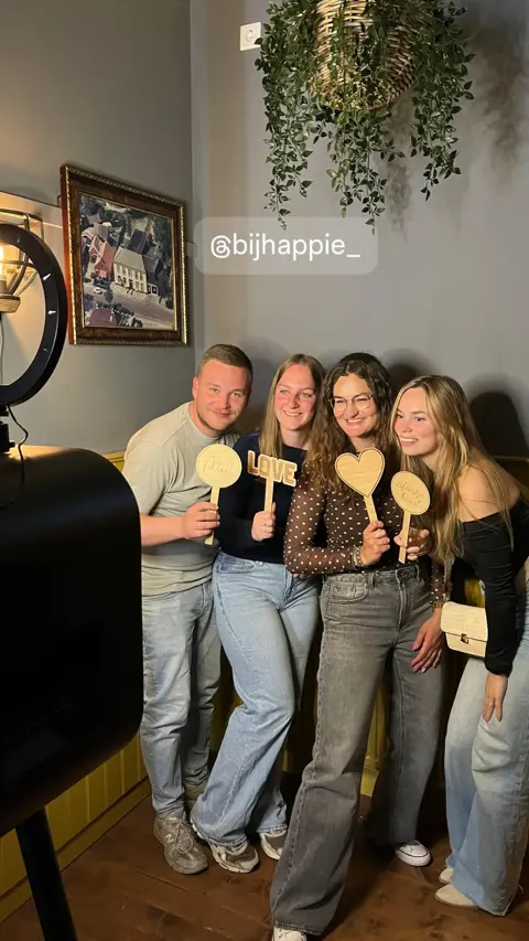 Vier gasten poseren met houten props naast de photobooth